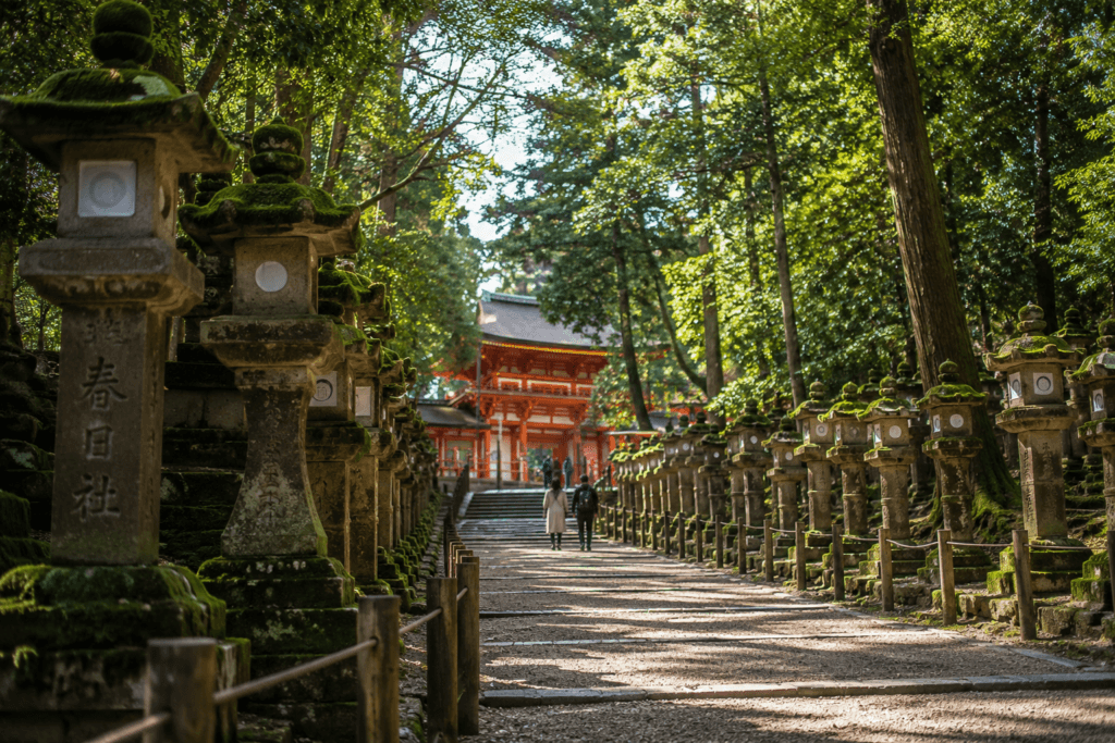 Kasuga Taisha-style forest path in Nara with moss-covered stone lanterns, sunlight through trees and a red shrine building in the distance