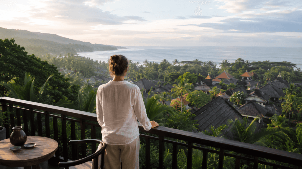Traveler overlooking tropical Bali rooftops, palm trees and the ocean from a hotel terrace