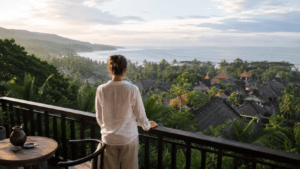 Traveler overlooking tropical Bali rooftops, palm trees and the ocean from a hotel terrace