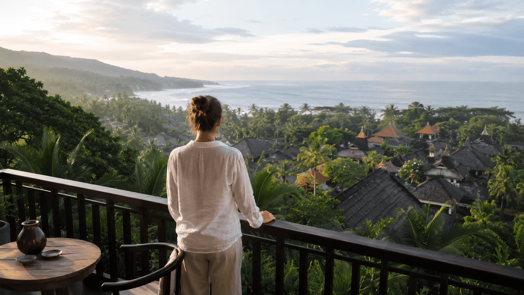 Traveler overlooking tropical Bali rooftops, palm trees and the ocean from a hotel terrace