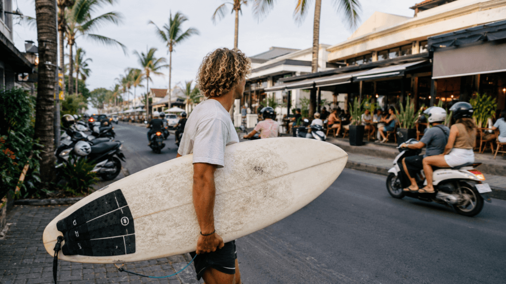 Surfer carrying a board along a busy cafe street in Canggu, Bali