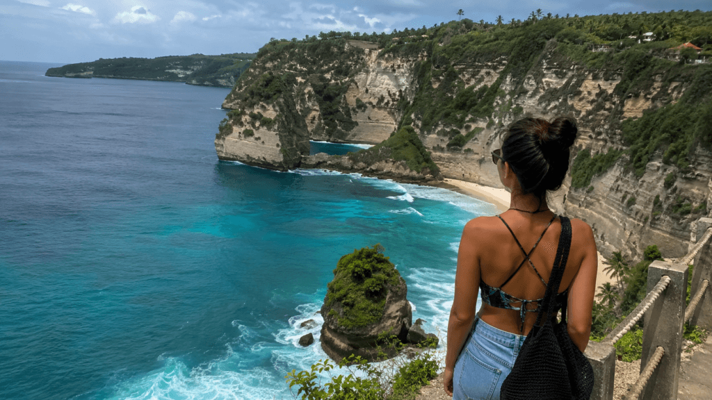 Traveler viewing turquoise water and limestone cliffs from an Uluwatu viewpoint in Bali