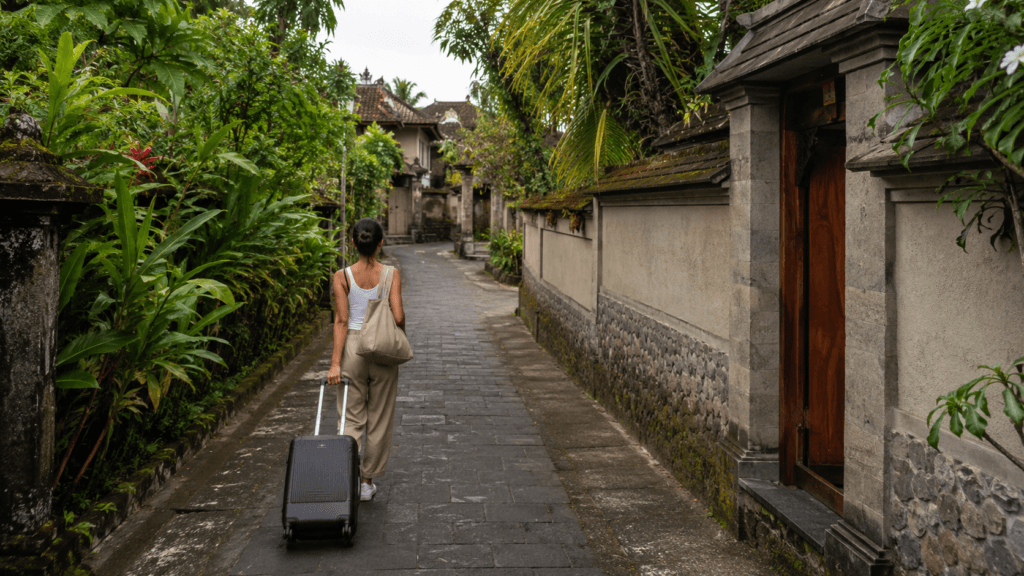Traveler pulling a suitcase along a narrow tropical lane toward a villa in Bali