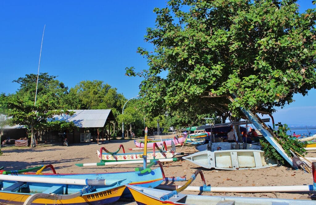 Colorful fishing boats beside shade trees on Sanur Beach in Bali