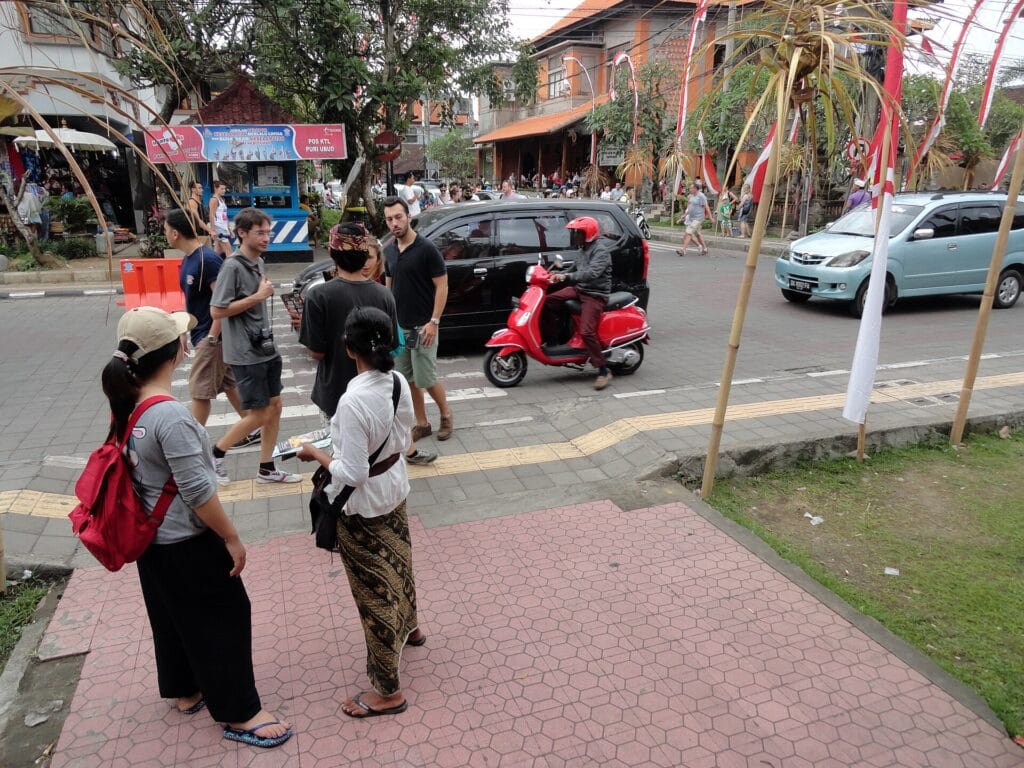 Travelers and scooters at the corner of Monkey Forest Road and Jalan Raya Ubud in Bali