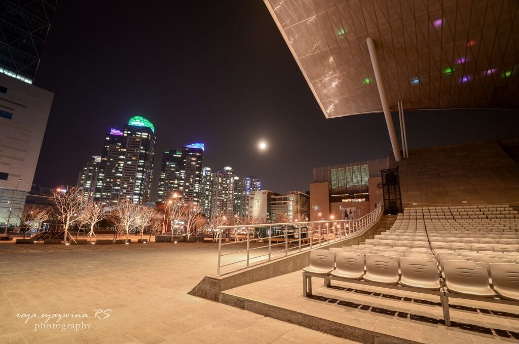 Outdoor seating beneath Busan Cinema Center with the Centum City skyline at night