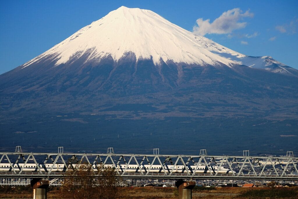 A Shinkansen train crossing a bridge beneath snow-covered Mount Fuji