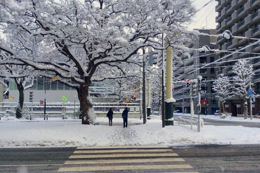 Two pedestrians walking beside a snow-covered street in Sapporo in November 2014
