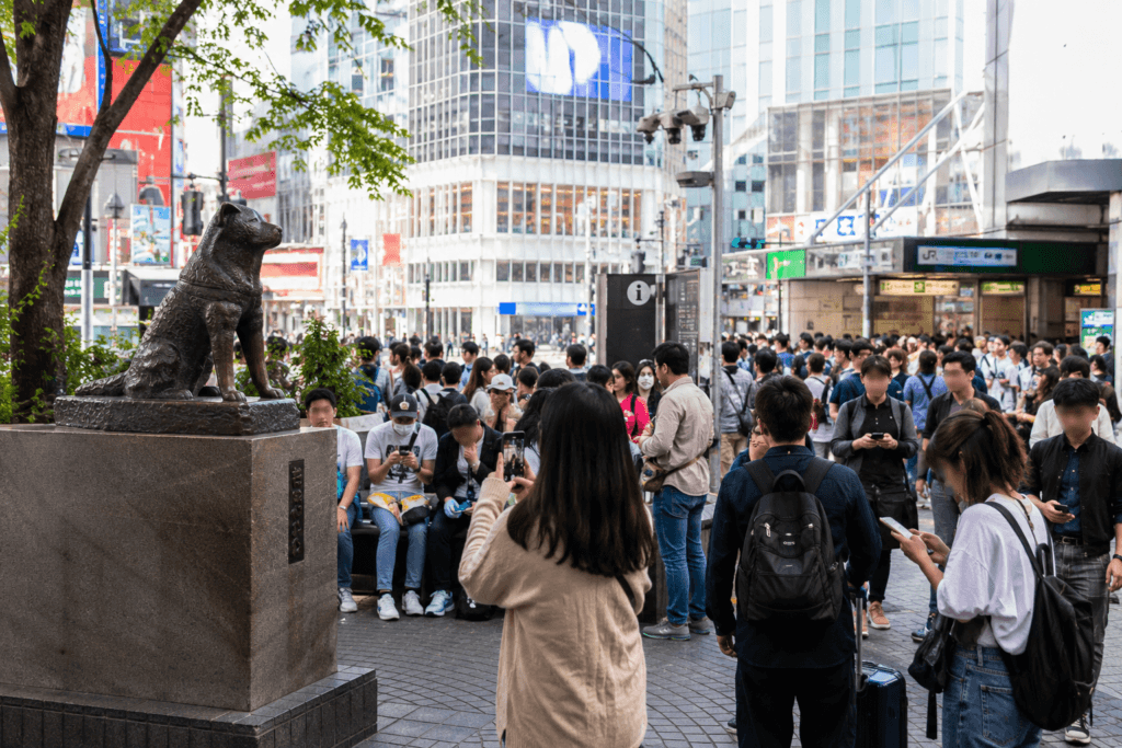 Busy Shibuya station meeting area with travelers near a small dog statue landmark